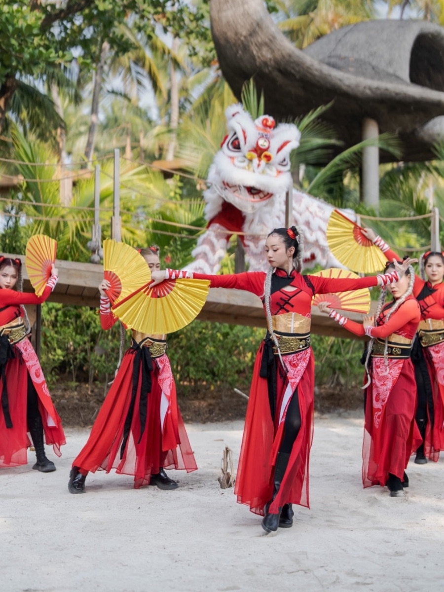Cultural dancers in red with fans, performing alongside a lion dance