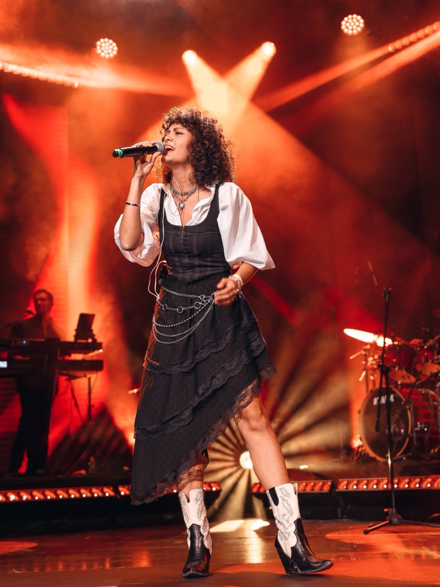 A singer performing live on stage under red lights