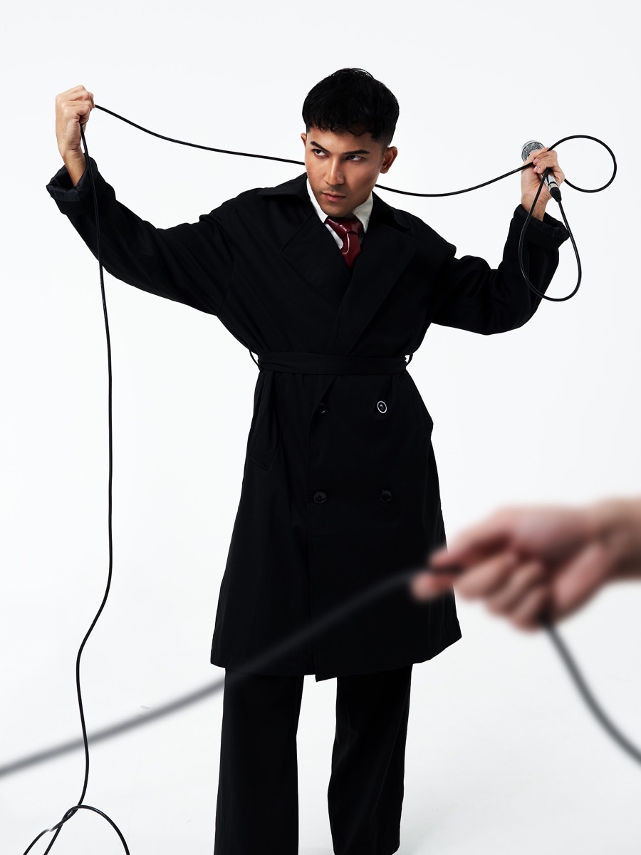 An emcee in a long black coat holding a microphone cable