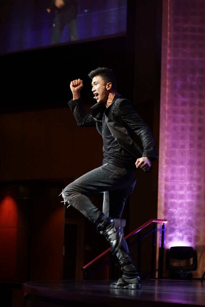A magician striking a pose on stage under purple light