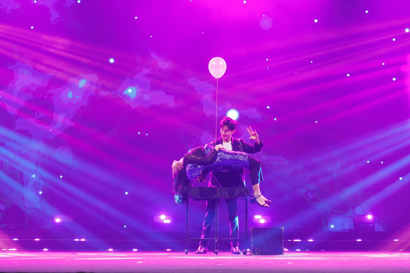 A levitation illusion under purple stage lights, with a floating balloon