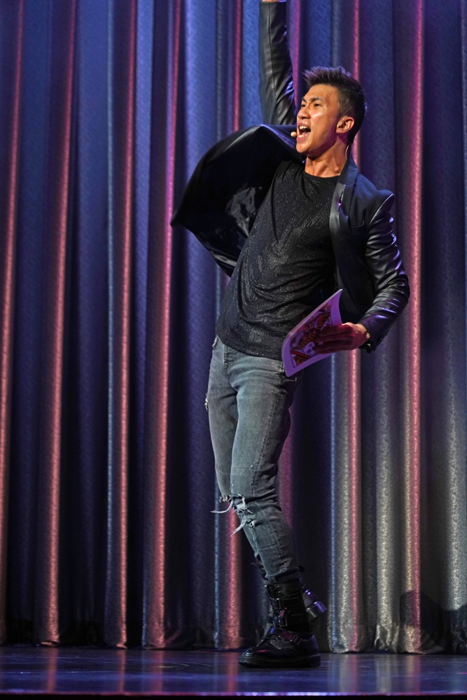 A magician celebrating on stage in front of a blue curtain