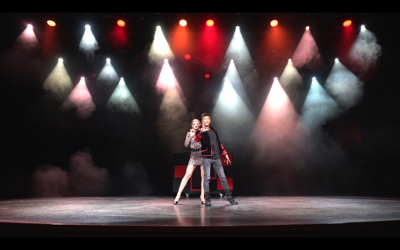 A magician and his partner on stage under coloured spotlights