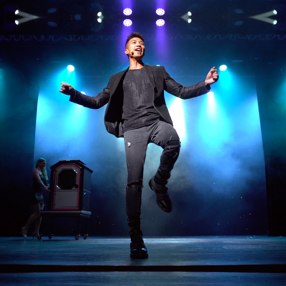 A magician leaping on stage under blue spotlights
