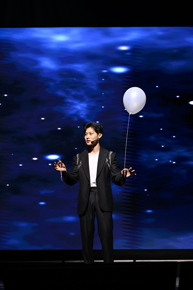 A magician on stage beside a floating white balloon